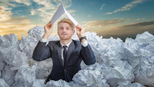 A man in a suit holds a paper aeroplane over a sea of crumpled papers, symbol bureaucracy, AI