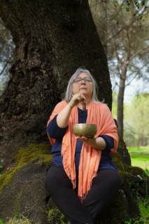 Mature woman with white hair in her sixties meditating in the forest with her eyes closed and a