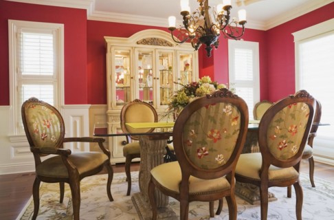 Glass top table with high-back wooden and upholstered chairs in dining room with buffet inside