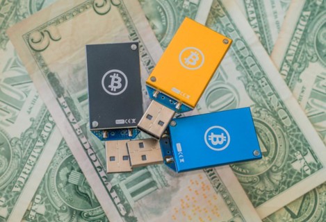 Blue and yellow USB hardware wallets with Bitcoin logos arranged on dollar bills, in South Korea