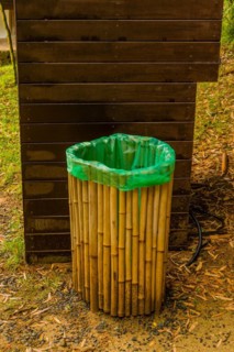 A green-topped trash can with a bamboo exterior stands beside a wooden board, in South Korea