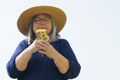 Smiling mature woman with white hair and hat with a bouquet of daisies in her hands isolated on a