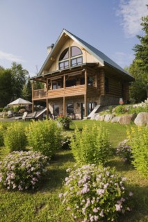 Handcrafted two story spruce log cabin home with fieldstone chimney and green sheet metal roof in