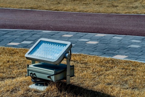 An LED floodlight installed on grass next to a paved path in daylight, in South Korea