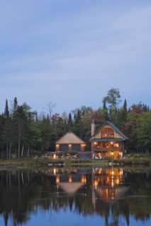 Illuminated two car garage and handcrafted two story spruce log cabin home with fieldstone chimney