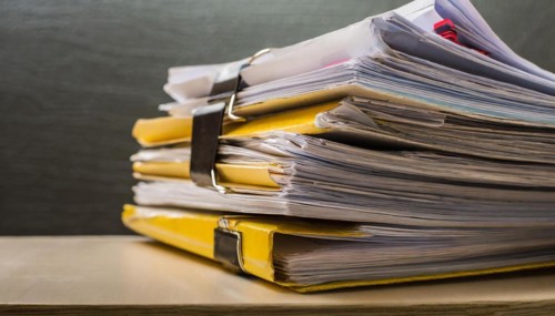 Folders with yellow tabs are piled up untidily on a table, symbolising bureaucracy, AI generated,