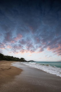 Lonely, wide sandy beach with turquoise-coloured sea. Tropical plants in a bay at sunset in the