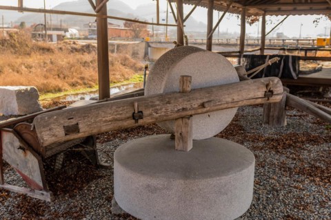 Old antique millstone and wheel in covered shelter with mountain community in background in South