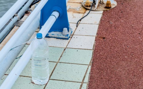 Discarded plastic bottle beside a metal railing on a mosaic tiled waterfront walkway, in Ulsan,