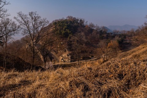 Section of mountain fortress wall behind leafless trees on top on winter morning with clear blue