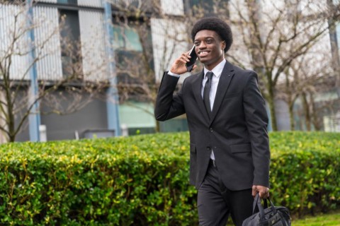 Three quarter length portrait of a cool smiling african businessman walking along the street using