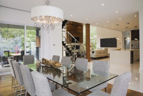 Glass dining table with gray upholstered high back chairs in dining room inside luxurious home,