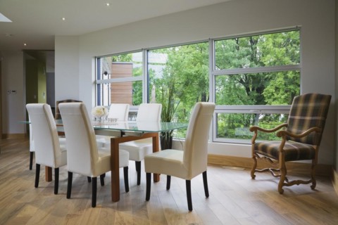 Clear glass top table with white leather high back chairs in dining room with beige ceramic tile