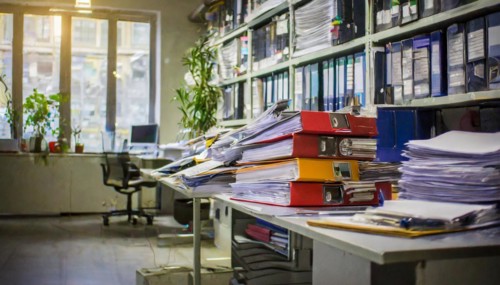 A busy office full of piles of documents and folders on shelves with a focus on organisation,