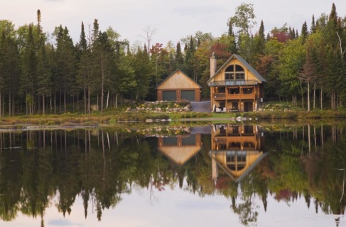 Garage and handcrafted two story spruce log cabin home with fieldstone chimney and green sheet