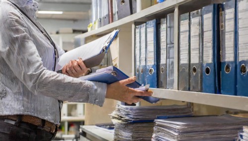 A woman works efficiently in the archive sorting files and paperwork, symbolism bureaucracy, AI