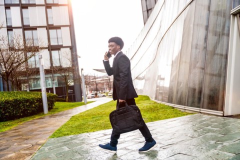 African businessman talking with mobile while commuting to work walking along the street