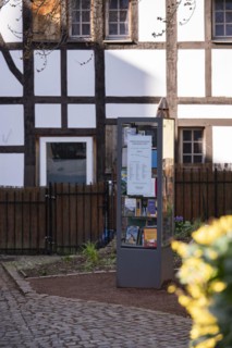 Bookcase in front of half-timbered house and fence, many colourful books in a glass display case,