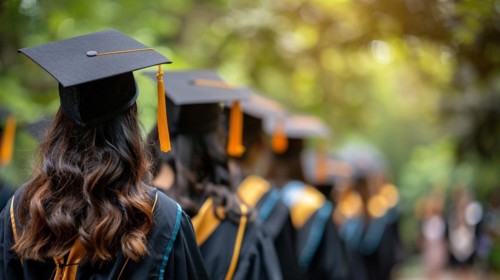 Graduates in a procession wearing caps and gowns, captured from behind, blurry out of focus