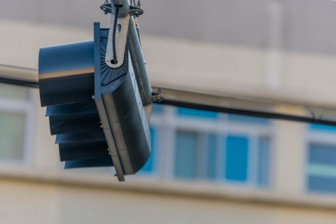 Bottom view of traffic light hanging from metal support with building blurred in background in