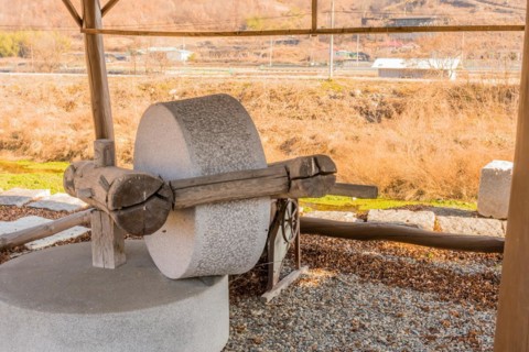 Old antique millstone and wheel in covered shelter with mountain community in background in South