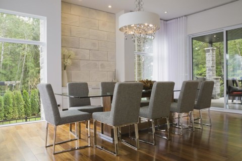 Glass dining table with gray upholstered high back chairs in dining room inside luxurious home,