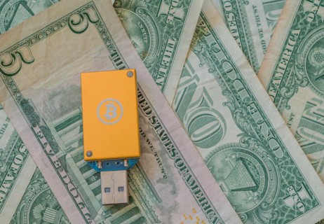 A yellow USB hardware wallet with a Bitcoin logo on a background of US dollar bills, in South Korea