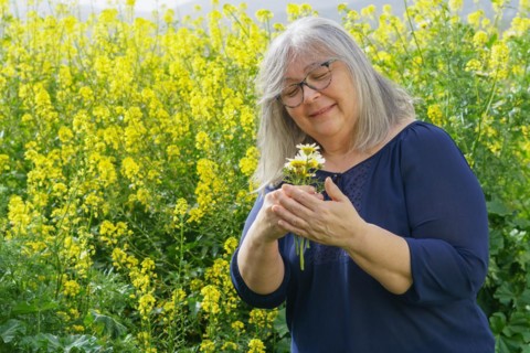 Smiling mature woman in her sixties with white hair and glasses holding a bouquet of daisies in her