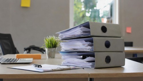 Black folders on a desk next to a laptop and a small plant, symbolising bureaucracy, AI generated,