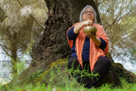 Mature woman with white hair meditating in the forest with her eyes closed and a Tibetan singing