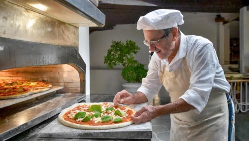 Pizza baker in Naples, Italy, preparing a pizza, in front of the pizza oven, AI generated, AI