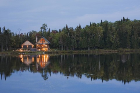 Illuminated two car garage and handcrafted two story spruce log cabin home with fieldstone chimney