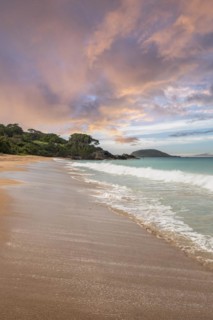 Lonely, wide sandy beach with turquoise-coloured sea. Tropical plants in a bay at sunset in the
