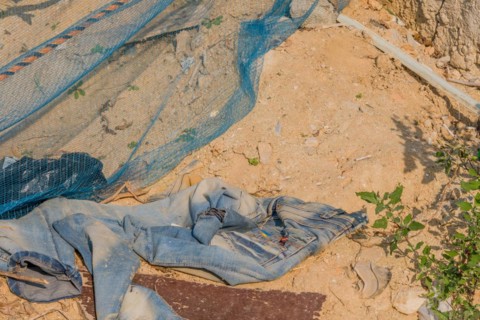 Discarded old clothes and a soil erosion net on dug up soil, showing environmental harm, in South