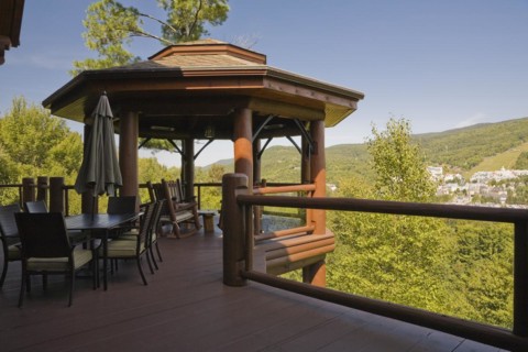 Brown stained gazebo on wooden deck with tempered glass and log railings attached to back of