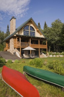 Handcrafted two story spruce log home cabin with fieldstone chimney, green sheet metal roof and red