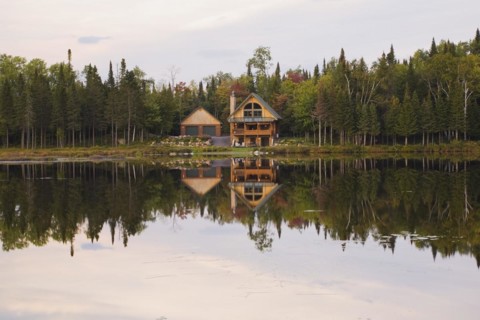 Garage and handcrafted two story spruce log cabin home with fieldstone chimney and green sheet