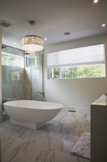Glass shower stall with white acrylic freestanding bathtub in main bathroom with marble floor tiles