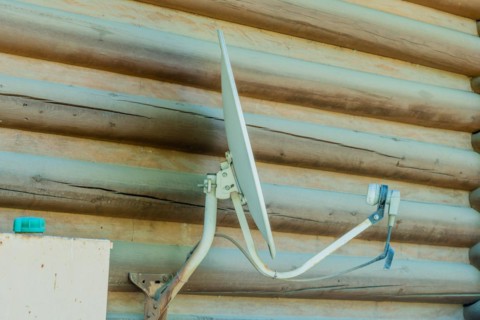 Satellite television receiver dish mounted on exterior wall of log cabin in South Korea