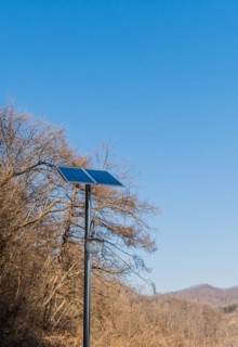 Small solar panel on top of chrome pole in front of leafless trees against blue sky in Buan, South