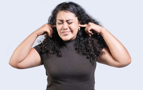 Frustrated young woman covering her ears ignoring something isolated. Displeased girl in glasses