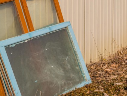 Leaning discarded window frames against a metal siding near weeds, in South Korea