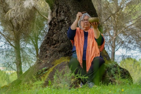 Mature woman with white hair meditating in the forest with her eyes closed and a Tibetan singing