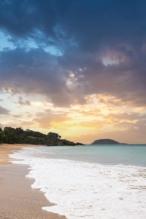Lonely, wide sandy beach with turquoise-coloured sea. Tropical plants in a bay at sunset in the