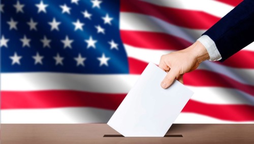 Hand holding ballot in voting ballot box with USA flag in background. USA presidential elections