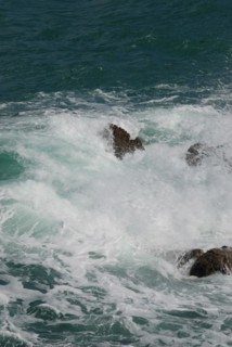 Turbulent waves crash against rocks, creating sea foam in the aquamarine ocean