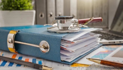Stethoscope on a pile of documents next to a laptop in the office, symbol bureaucracy, AI
