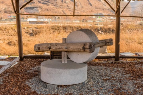 Old antique millstone and wheel in covered shelter with mountain community in background in South