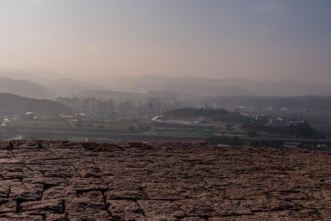 Top of mountain fortress wall made of flat stones with rural community under hazy sky in background