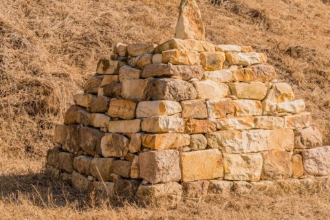 Closeup of pyramid shaped rock structure in field of brown grass at foot of hillside in Boeun,